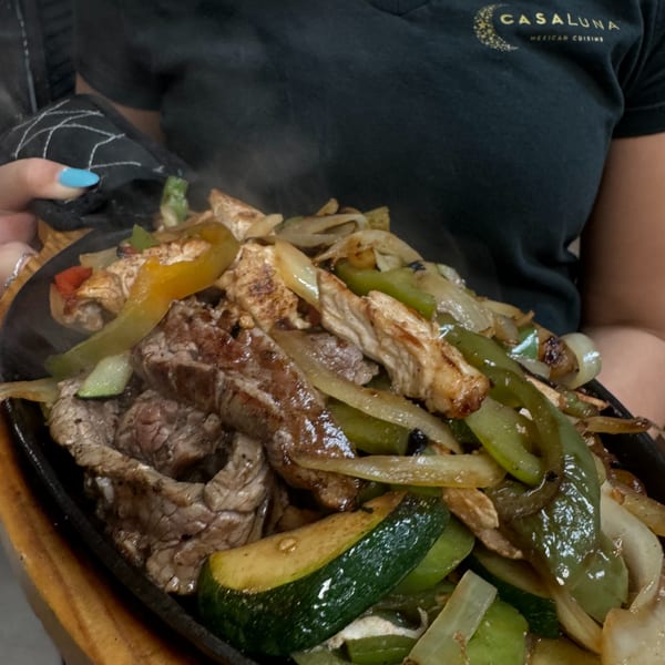 Sizzling fajitas with steak, chicken, bell peppers, onions, and zucchini on a hot plate.