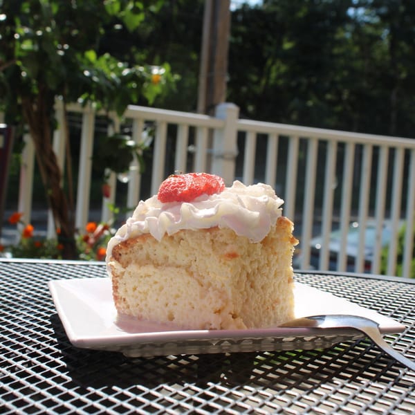 Slice of Tres Leches cake with whipped cream and a strawberry on an outdoor patio table.