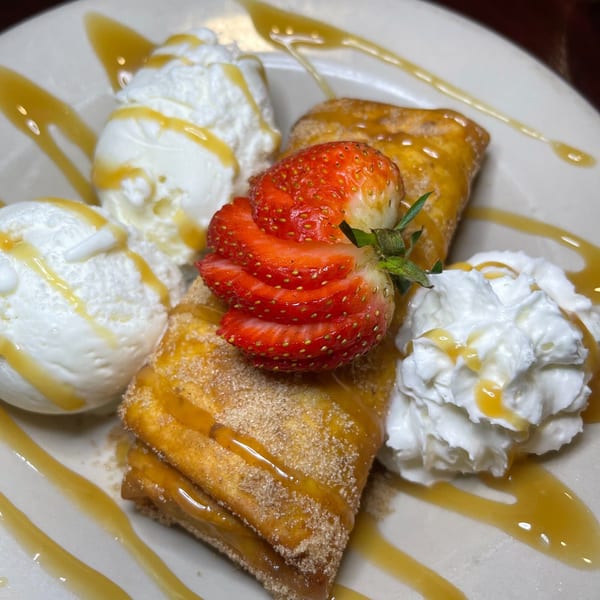 Two golden-brown Mexican dessert pastries with ice cream, whipped cream, sliced strawberries, and caramel drizzle.