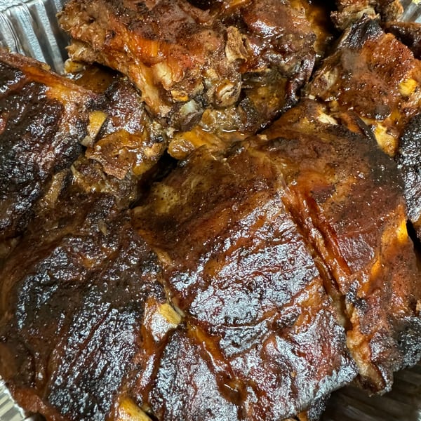 Close-up of glistening, dark brown, saucy ribs in a foil pan, ready to be served.
