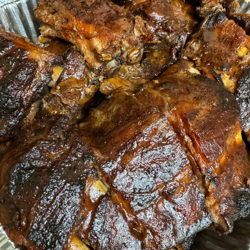 Close-up of glistening, dark brown, saucy ribs in a foil pan, ready to be served.
