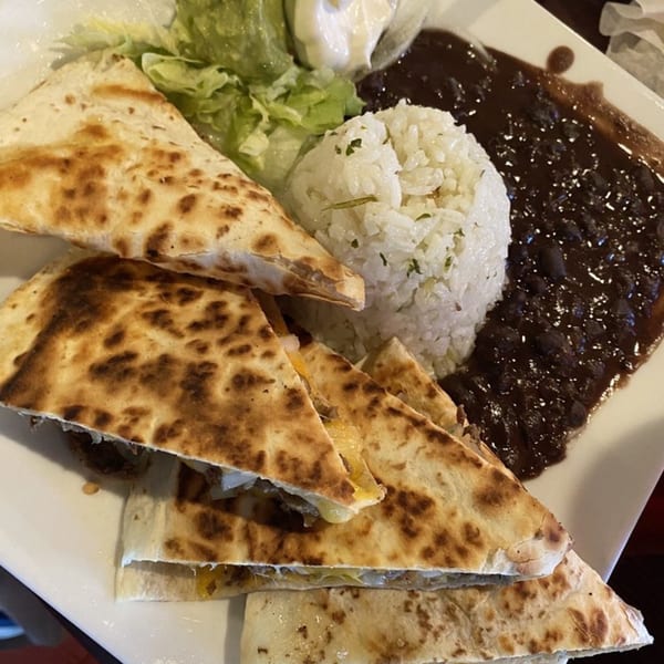 A plate of Casa Luna's quesadillas, rice, black beans, and a side salad with sour cream.
