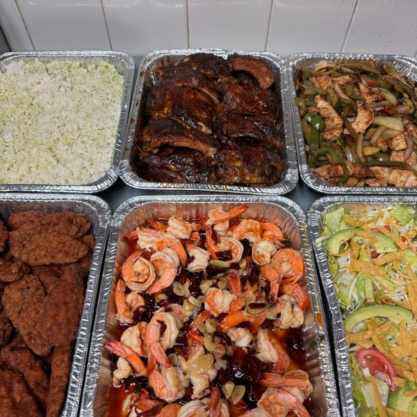 A catering spread of Mexican dishes including rice, ribs, fajitas, fried chicken, shrimp, and salad.