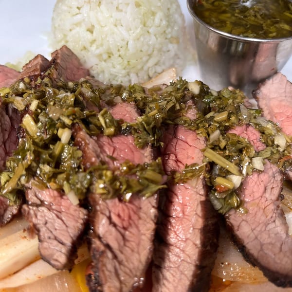 Sliced steak with green chimichurri sauce, white rice, and a side of green sauce.