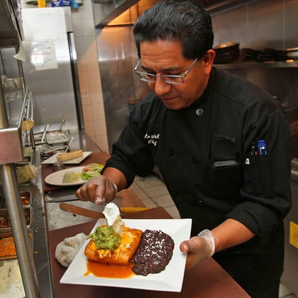 Chef Raziel plating a Mexican dish with a burrito, black beans, guacamole, and sour cream.