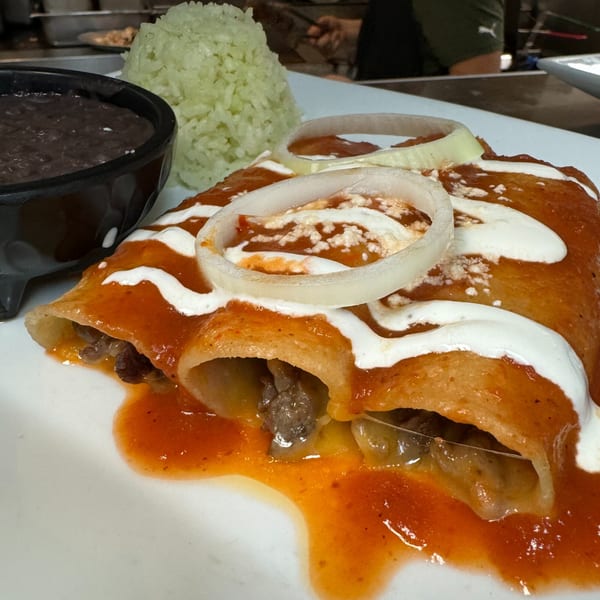Three beef enchiladas topped with red sauce, sour cream, and onion, served with rice and beans.