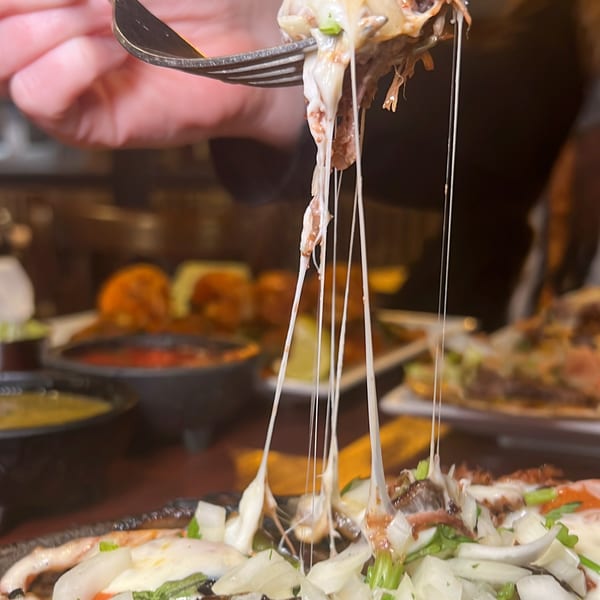 A fork lifts cheesy, meaty Mexican food, creating long, gooey cheese pulls above a dish of food.