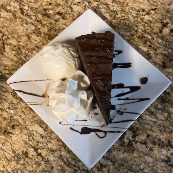 A slice of rich chocolate cake with vanilla ice cream and whipped cream on a white plate.