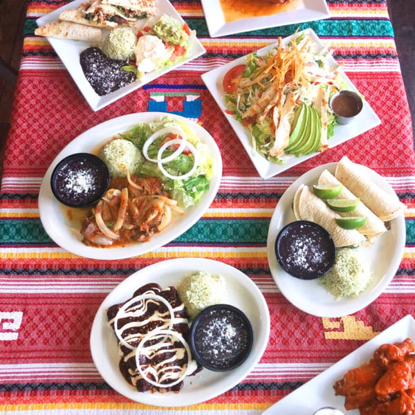 A vibrant table spread of various Mexican dishes, including tacos, enchiladas, and salads, on a colorful striped tablecloth.