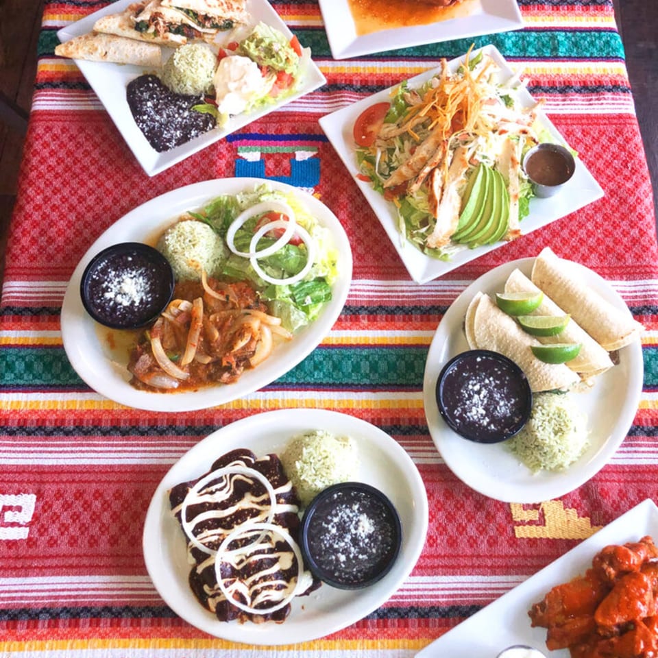 A vibrant table spread of various Mexican dishes, including tacos, enchiladas, and salads, on a colorful striped tablecloth.