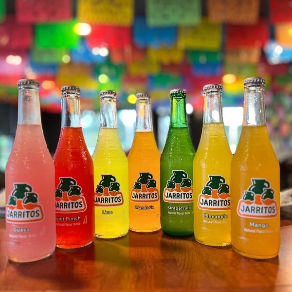 Seven colorful Jarritos sodas, including Guava, Fruit Punch, Lime, Mandarin, Grapefruit, Pineapple, and Mango.