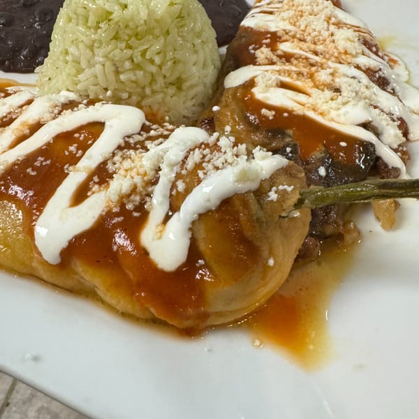Two chili rellenos topped with red sauce, crema, and cheese, served with green rice and black beans.