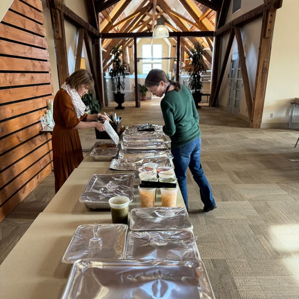 Two women setting up a buffet of Casa Luna Mexican Cuisine dishes in a large room.
