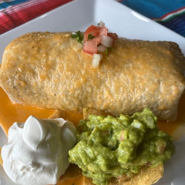 A large Casa Luna Mexican Cuisine burrito covered in cheese sauce, with guacamole and sour cream.