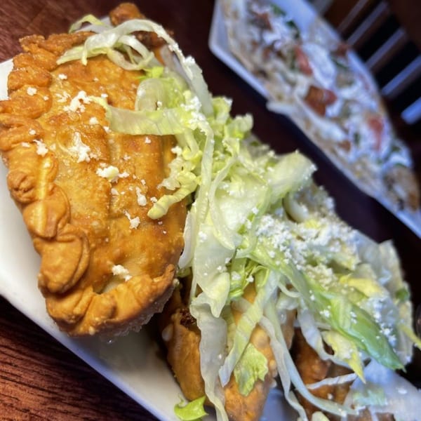 Golden-brown empanadas topped with shredded lettuce and crumbled white cheese on a white plate.